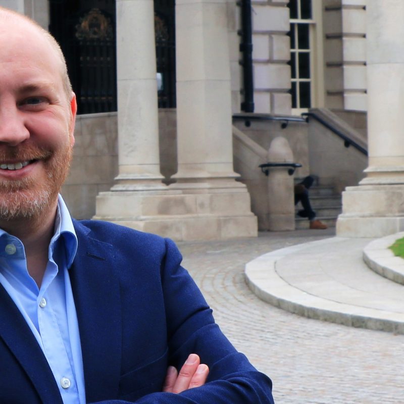 Steven Agnew, head of RenewableNI, standing in front of Belfast city hall. he is wearing a suit and his arms are crossed