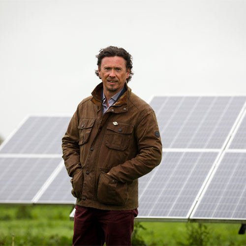 Paul Carson stands with his hands in coat pockets in front of solar panels